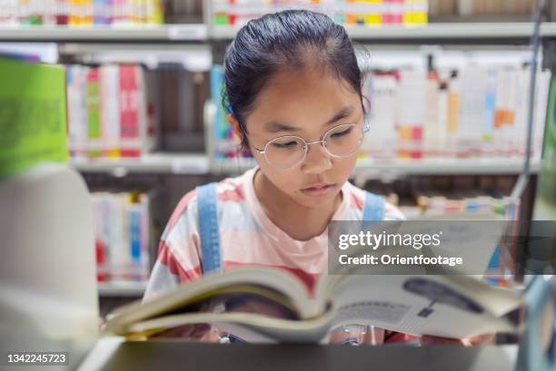 bambina che legge un libro sulla libreria in biblioteca - miopia foto e immagini stock