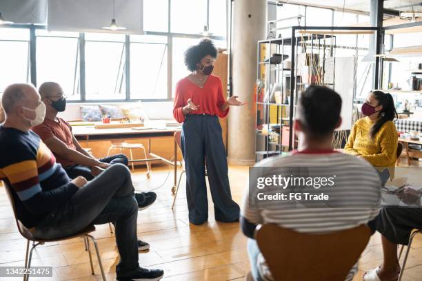 young woman talking in group therapy at a coworking - wearing a face mask - business strategy covid stock pictures, royalty-free photos & images