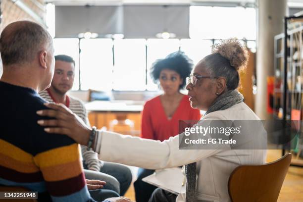 senior woman comforting a mature man in group therapy at a coworking - gruppterapi bildbanksfoton och bilder