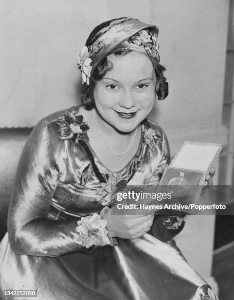 Norwegian figure skater and actress Sonja Henie , wearing an outfit decorated with flowers and a matching hat, poses with her ladies' singles gold...