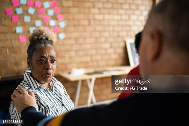 senior woman talking and crying in group therapy - upset coworker stock pictures, royalty-free photos & images