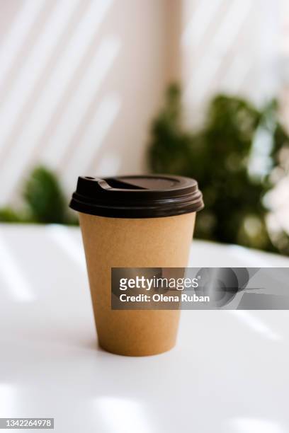 disposable coffee cup on table with plants on background. - takeaway coffee stockfoto's en -beelden