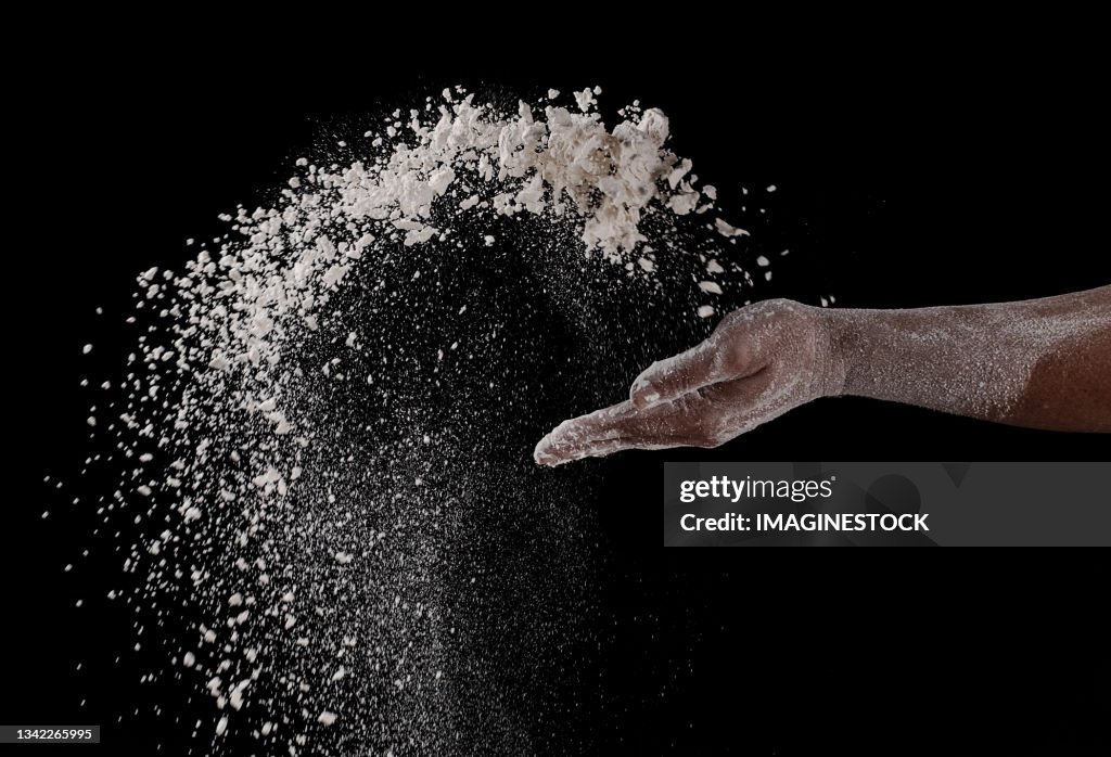 Close-up of a hand throwing flour on a black background
