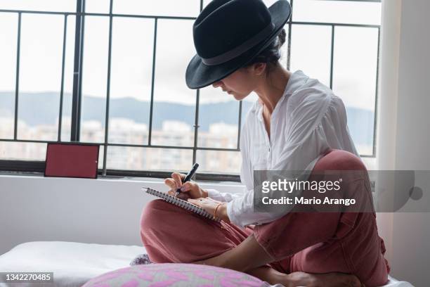 beautiful woman sitting by the window writing to a poet enjoying her hobby - poet stock pictures, royalty-free photos & images