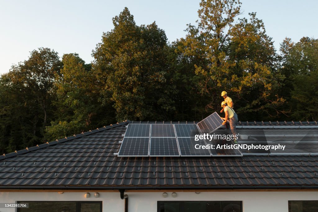 Zwei Arbeiter installieren Sonnenkollektoren auf dem modernen Haus.