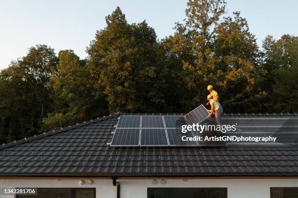 zwei arbeiter installieren sonnenkollektoren auf dem modernen haus. - solar stock-fotos und bilder