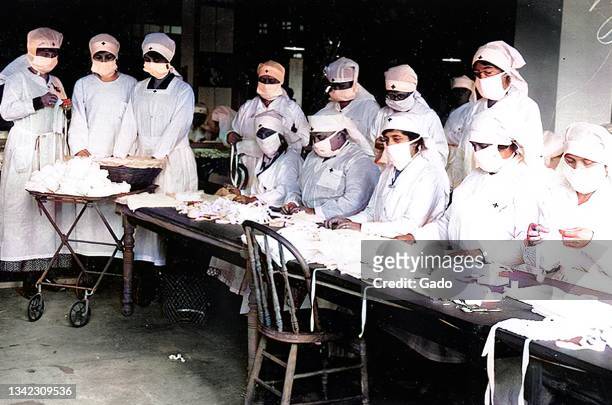 Red Cross volunteers assemble gauze face masks to prevent the spread of influenza while wearing masks themselves during the 1918 flu pandemic,...
