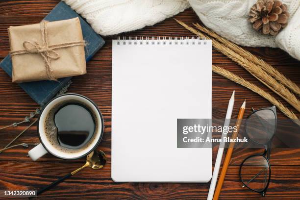 vintage style still life: craft envelopes, blank note pad with copy space, gift box, pencils, eyeglasses, flowers and book over dark brown natural wood background. - coffee table from above stock-fotos und bilder