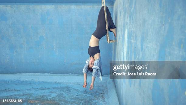 portrait of young woman upside down against empty blue swimming pool background - hallenbad leer stock-fotos und bilder