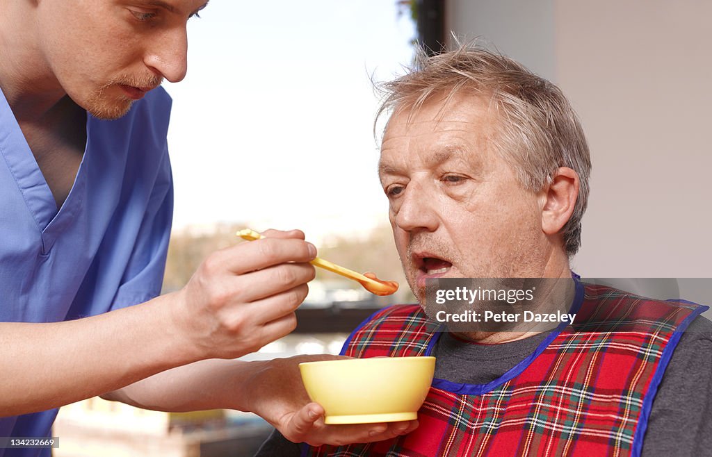 Senior man getting fed by carer in care home