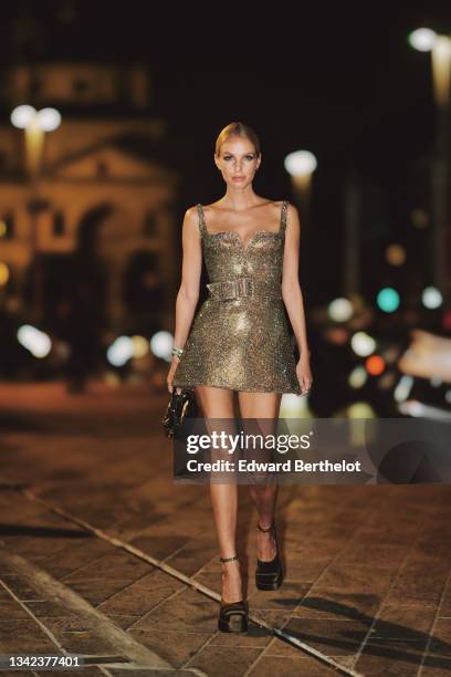 Leonie Hanne wears silver earrings, a green / pink / white shiny full rhinestones V-neck / tank-top / belted short dress, a gold Juste Un Clou...