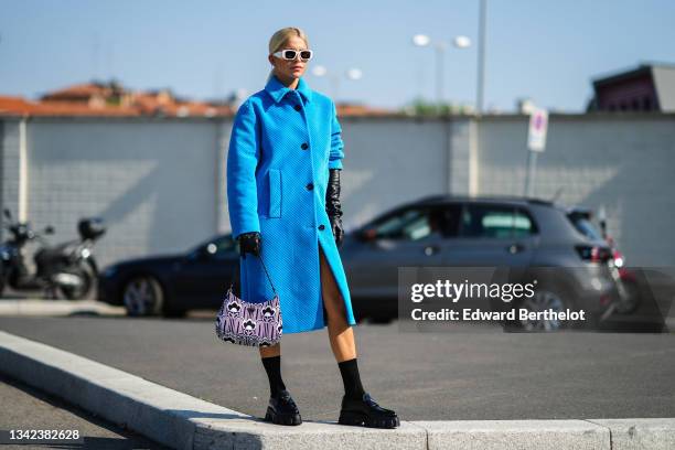 Caroline Daur wears white Prada sunglasses, earrings, a blue shiny ribbed velvet short sleeves long Prada coat, black shiny leather long gloves from...