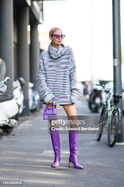 Leonie Hanne wears purple sunglasses, a green mint and purple pattern wool turtleneck oversized pullover dress, a purple shiny leather Chiquito...