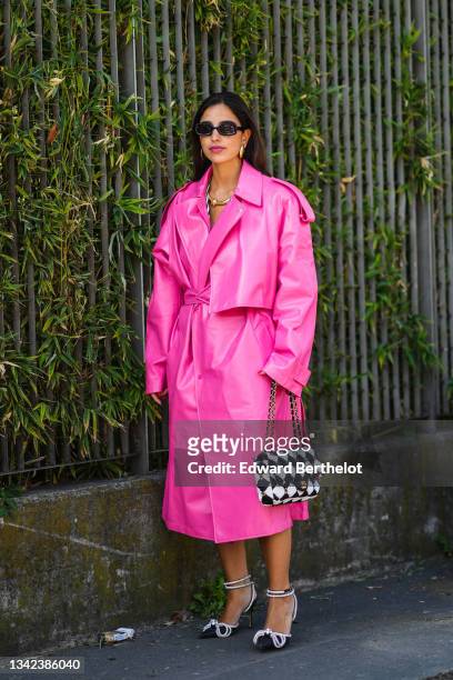 Bettina Looney wears black sunglasses, gold large earrings, a pink shiny leather oversized long belted coat, a black and white checkered quilted...