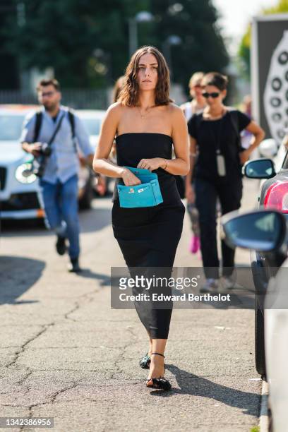 Erika Boldrin wears a black shoulder-off midi tube dress, a blue shiny leather Kelly handbag from Hermes, black shiny leather fringed asymmetric...