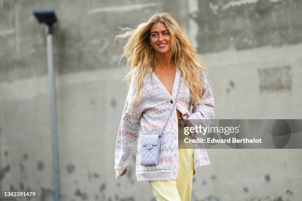 Emili Sindlev wears a white with red / yellow / purple print pattern wool long oversized cardigan, a pale purple shiny grained leather crossbody bag...