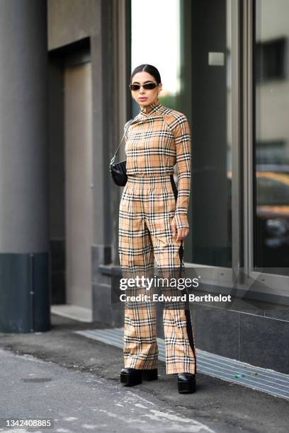 Guest wears black sunglasses, silver earrings, a beige with red / white / black checkered print pattern high zipper neck long sleeves pullover from...