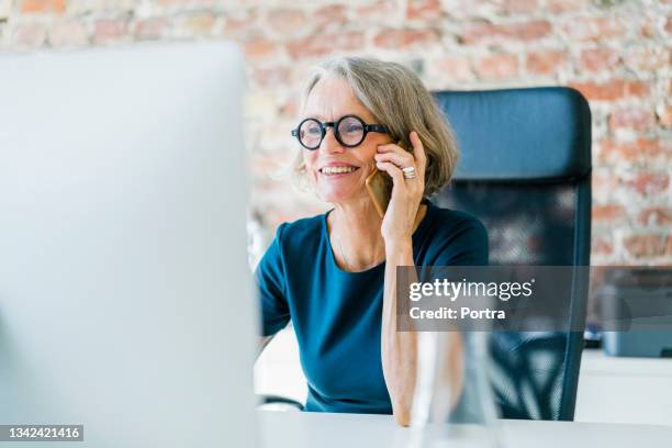 senior businesswoman at her desk using cell phone - friendly business phonecall stockfoto's en -beelden