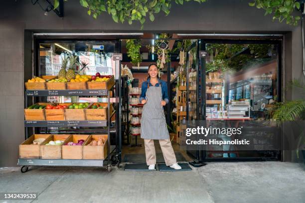 donna felice che lavora in un mercato alimentare locale e in piedi alla porta in attesa dei clienti - bottega foto e immagini stock