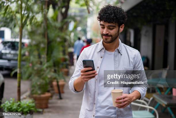 homem feliz em movimento bebendo uma xícara de café em movimento enquanto verificava seu celular - handsome mexican men - fotografias e filmes do acervo