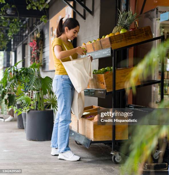 compradora que compra frutas en una tienda de comestibles local con una bolsa reutilizable - stand alone fotografías e imágenes de stock