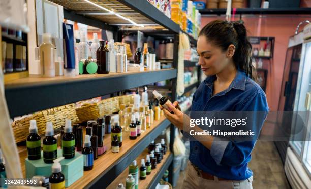 woman shopping at an organic market and looking at supplements - cosmetic bottle stockfoto's en -beelden
