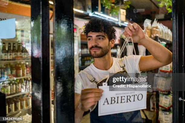 man hanging an open sign at a local supermarket - open sign stockfoto's en -beelden