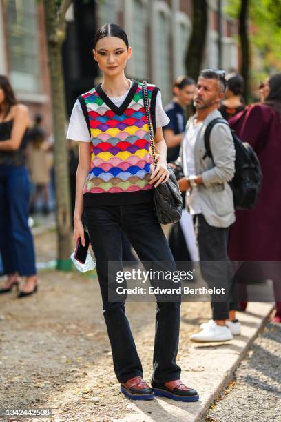 Guest wears a white t-shirt, a multicolored flashy print pattern V-neck / sleeveless pullover, black pants, a black shiny leather Chanel 19 shoulder...