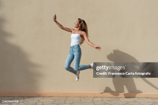 woman taking selfie through smart phone while jumping - blonde woman selfie stockfoto's en -beelden