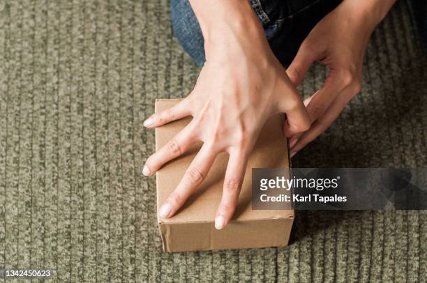 a young southeast asian woman is unboxing a package delivery carton box on the bed - unboxing - fotografias e filmes do acervo
