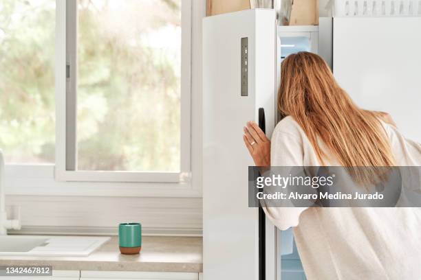 young pretty woman in casual clothes looking inside her refrigerator in the kitchen. - refrigerator stock-fotos und bilder