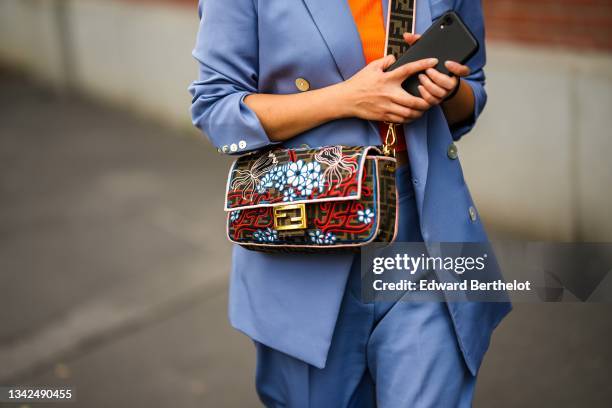 Guest wears a neon orange ribbed turtleneck pullover, a purple blue long blazer jacket, matching purple blue large pants, a brown and beige FF...