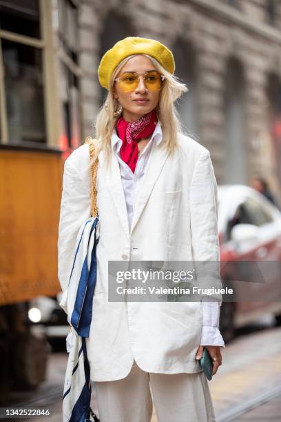 Guest outside Ermanno Scervino fashion show wearing a white pant suit, yellow berret, red bandana around the neck, orange sunglasses and Gucci bag...