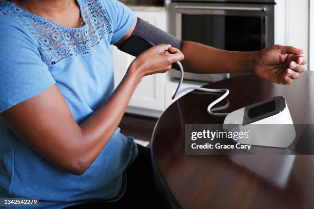 woman adjusts cuff on upper arm blood pressure monitor - blood pressure stock-fotos und bilder