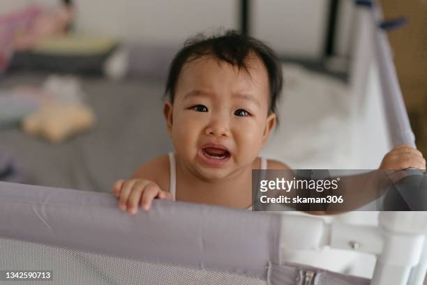 asian baby girl (4-7month)standing feeling negative emotion and crying and shouting in baby playpen fence - crying toddler stock pictures, royalty-free photos & images