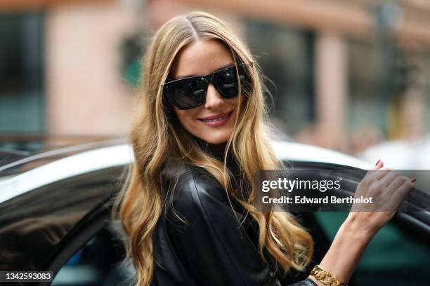 Olivia Palermo wears black sunglasses, earrings, a black oversized belted midi leather dress with leather cut-out flower pattern yoke, outside the...