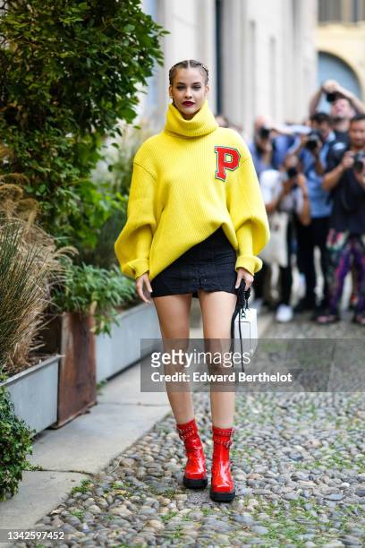 Barbara Palvin wears a gold chain hair clip, a yellow ribbed wool oversized pullover with a red P embroidered from Philosophy, a black denim lace...