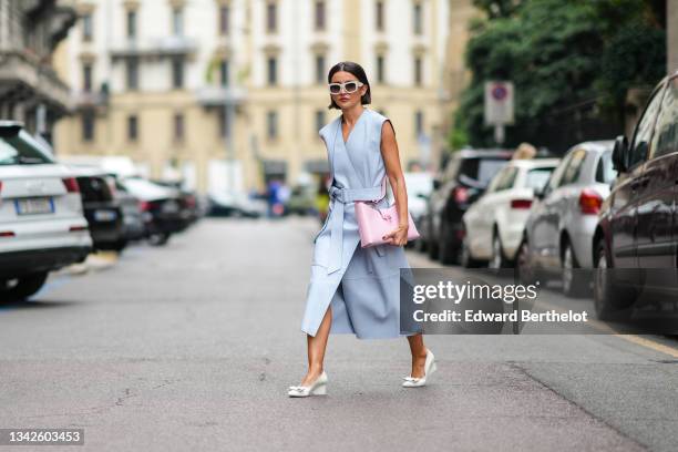 Alexandra Pereira wears white sunglasses, silver and rhinestones earrings, a pale blue shiny leather V-neck / sleeveless / belted / slit midi dress,...