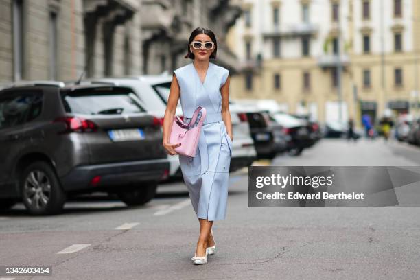 Alexandra Pereira wears white sunglasses, silver and rhinestones earrings, a pale blue shiny leather V-neck / sleeveless / belted / slit midi dress,...