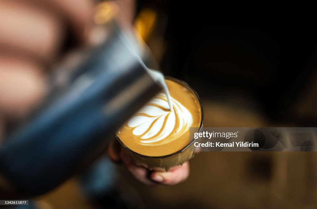 Nahaufnahme der Hand gießen Kaffee Latte Kunst