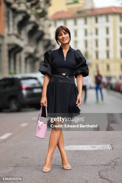 Carlotta Rubaltelli wears gold earrings, a black puffy sleeves / zipper neck / flowing dress, a black nylon Prada belt, a silver ring, a pale pink...