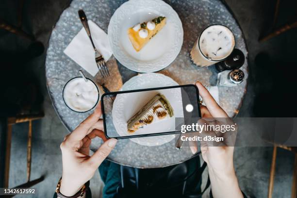 overhead view of young woman taking photos of her delicious looking green tea crepe cake with smartphone before eating it in coffee shop. eating out lifestyle. camera eats first culture - internet café stock-fotos und bilder