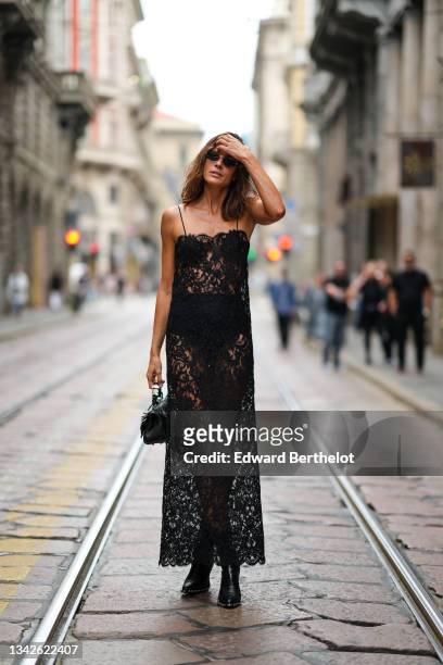 Chiara Baschetti wears sunglasses, a black cut-out and embroidered lace flower pattern tank-top / long dress, a black shiny leather fringed handbag,...