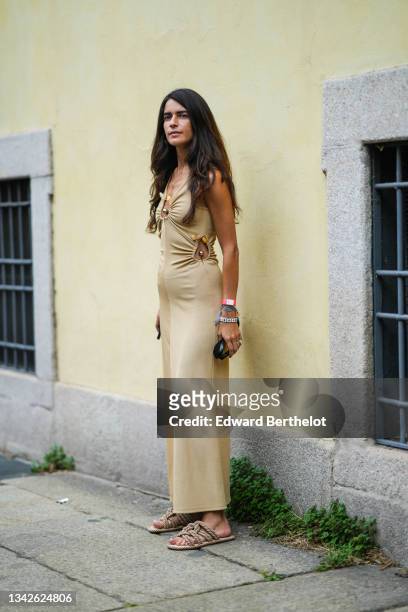 Chiara Totire wears a gold chain pendant necklace, a beige ribbed V-neck / cut-out flowing long dress with silver and yellow stones, a white with...