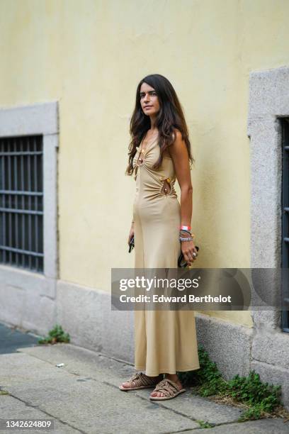 Chiara Totire wears a gold chain pendant necklace, a beige ribbed V-neck / cut-out flowing long dress with silver and yellow stones, a white with...