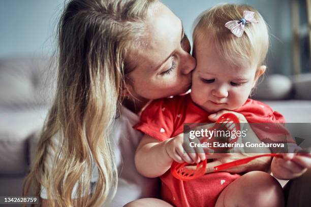 a young mother hugs her 1-year-old daughter in a red fluffy dress at home - red dress child stock pictures, royalty-free photos & images