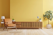 Cabinet TV in modern living room with leather armchair and plant on yellow wall background.