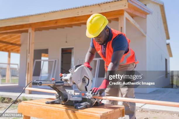 african american worker sawing plank during wood frame house construction - power tool stock pictures, royalty-free photos & images