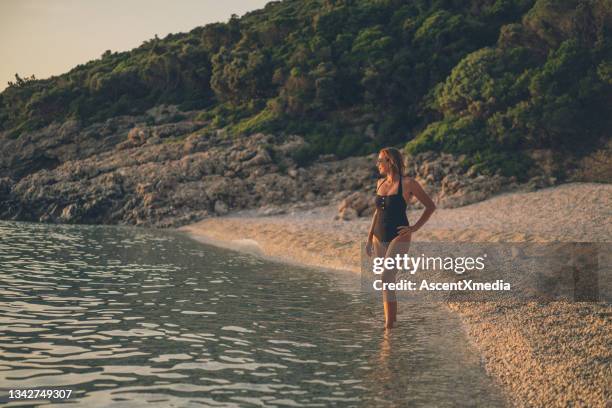 woman walks down sandy beach at sunrise - middle aged woman bathing suit stock pictures, royalty-free photos & images