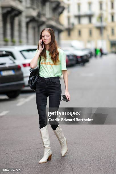 Model wears a pale green with orange inscription t-shirt from Salvatore Ferragamo, high waist black denim skinny jeans pants, a black shiny leather...